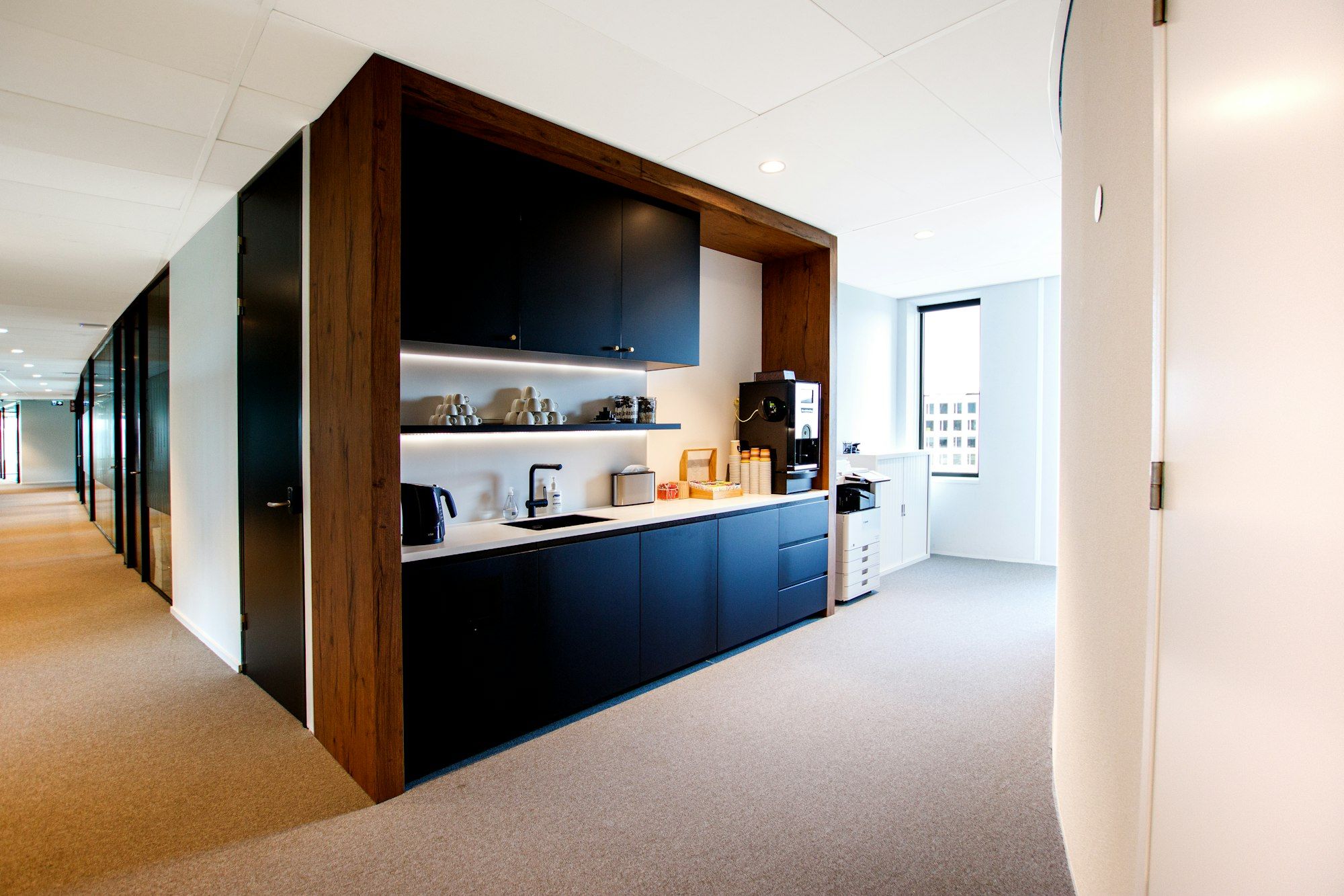 Moderne Büro-Teeküche mit dunklen Fronten, heller Arbeitsfläche und Kaffeemaschine