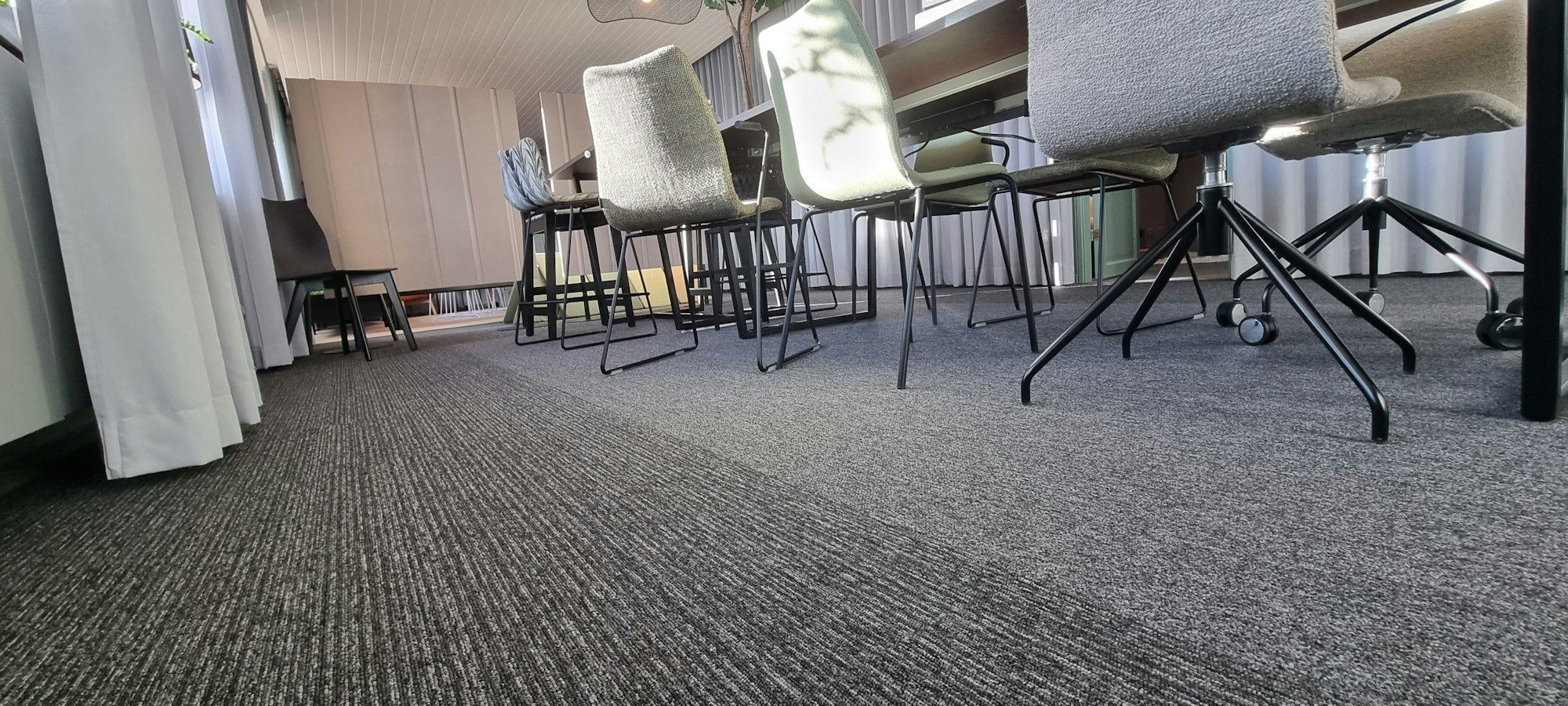 Grauer Teppichboden in einem Büro mit hellen Stühlen und schwarzen Stuhlbeinen
